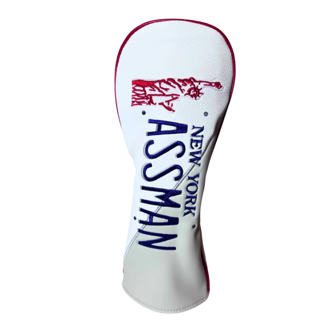 A red and white ASSMAN golf head cover with 'ASSMAN' written in bold blue letters and a graphic of the Statue of Liberty in red.